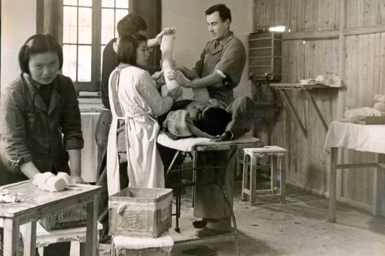 Medical personnel examine a patient who is lying on a table, leg bent up in the air.