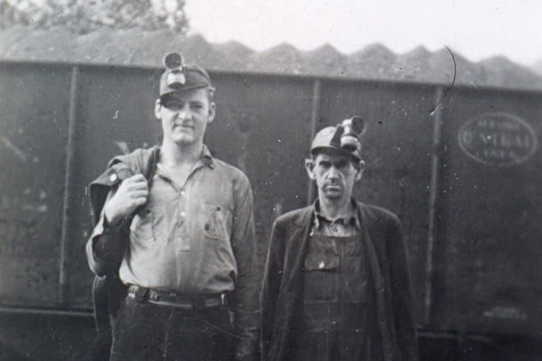 Two coal miners standing next to a train car carrying coal