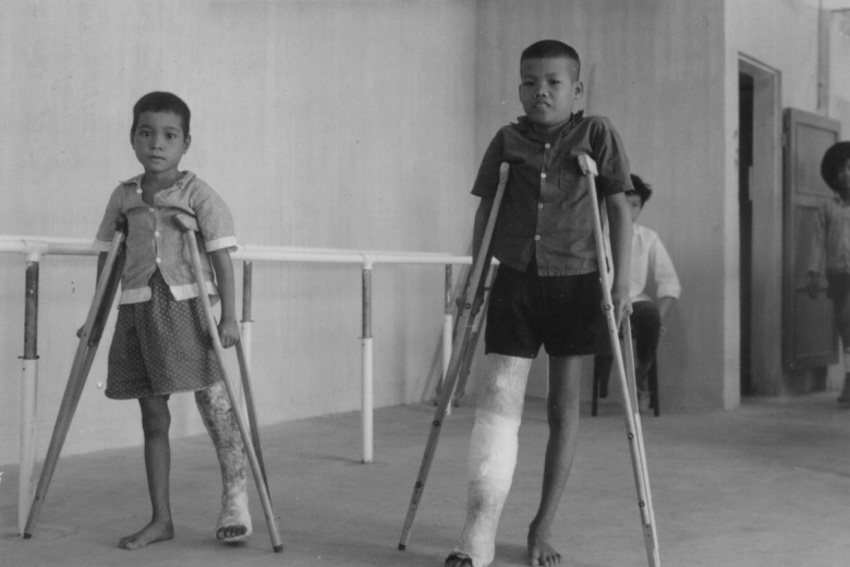 Two children with prosthetic legs walk with the aid of crutches.
