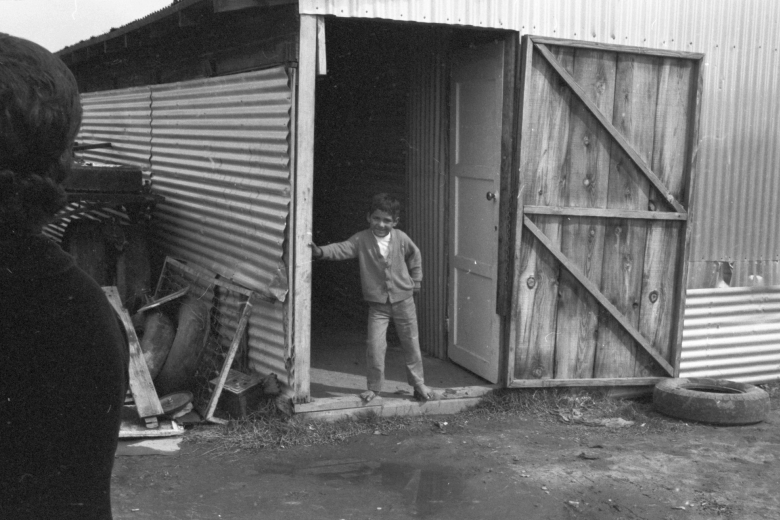 Boy stands in the doorway of a home made out of tin and wood.