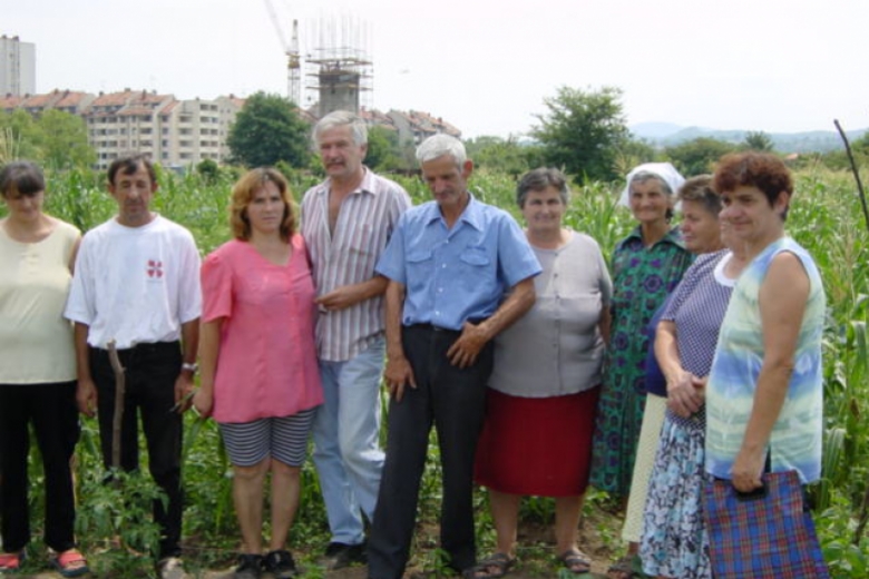 Nine people stand together in a field with buildings in the background.
