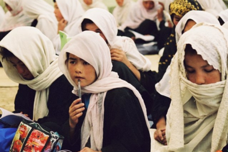 Young women sit together in lines, facing forward, one woman with a pen pressed up to her lip.