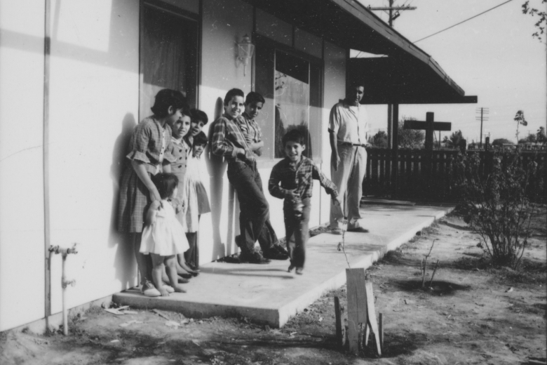 Man and children stand and play on the porch of a house.