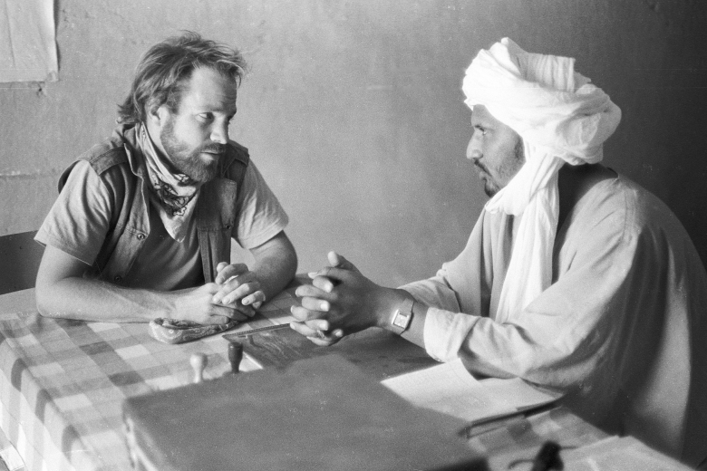Two men sitting across the table from one another, talking.