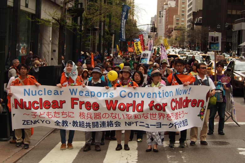 Group of protesters sanding in a street holding a sign written in both Japanese and English, "Nuclear weapons convention now! Nuclear free world for children."