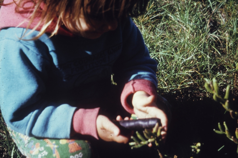 Child squats in the grass holding a small, brown cylinder.