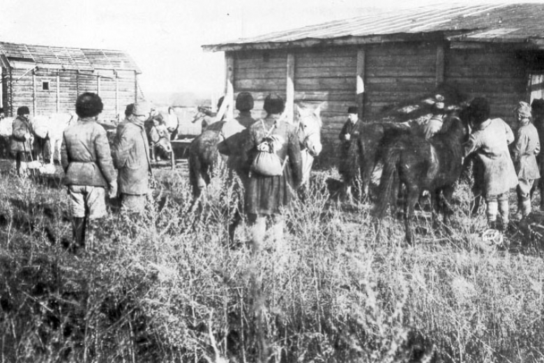 Men wait in line in front of horses and building.