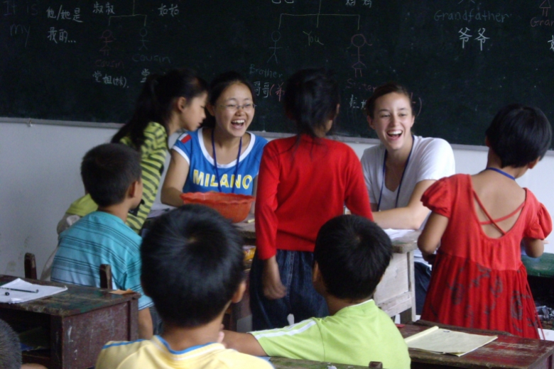 Eight children laugh together in a classroom in front of a blackboard.