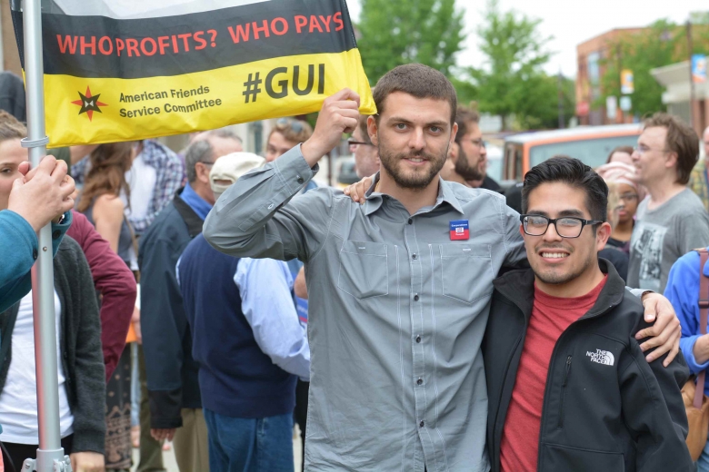 Two men stand in a crowd with a banner to their side.