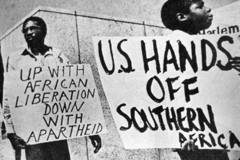 Two people hold signs that read "U.S. Hands Off Southern Africa" and "Up with African Liberation Down with Apartheid."