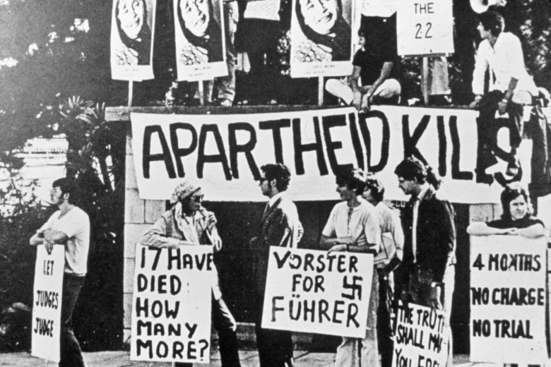 Group of people holding signs and banners, one of which reads "Apartheid kills."