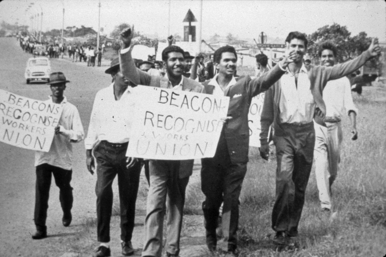 Group of men walk together holding signs and with hands raised in celebration.