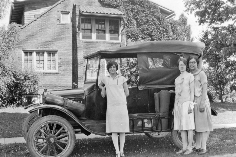 Three women standing in front of a car.