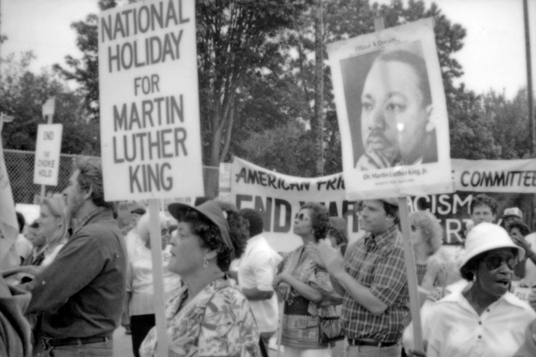 Group of people cheer and clap while holding signs referencing Dr. Martin Luther King.