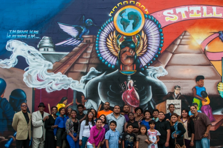 Multi-age group stands in front of a colorful mural.