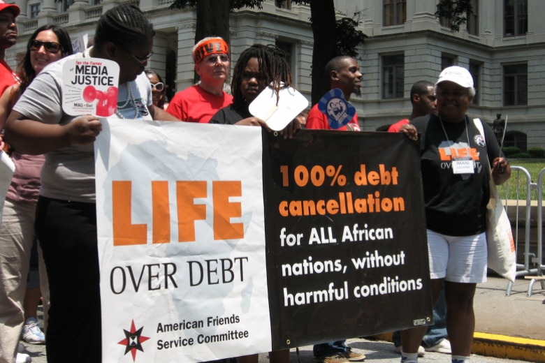 Group of people walk together, holding a banner that reads "Life over debt."