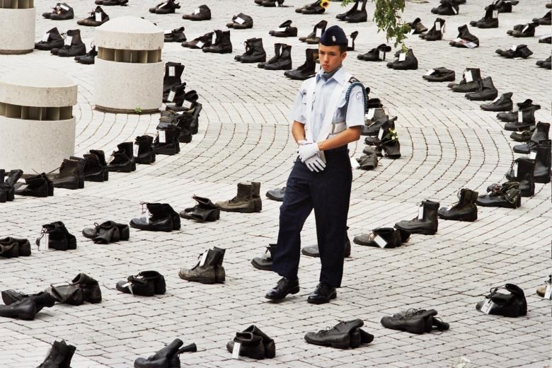 Man wearing military uniform walks among rows of boots.
