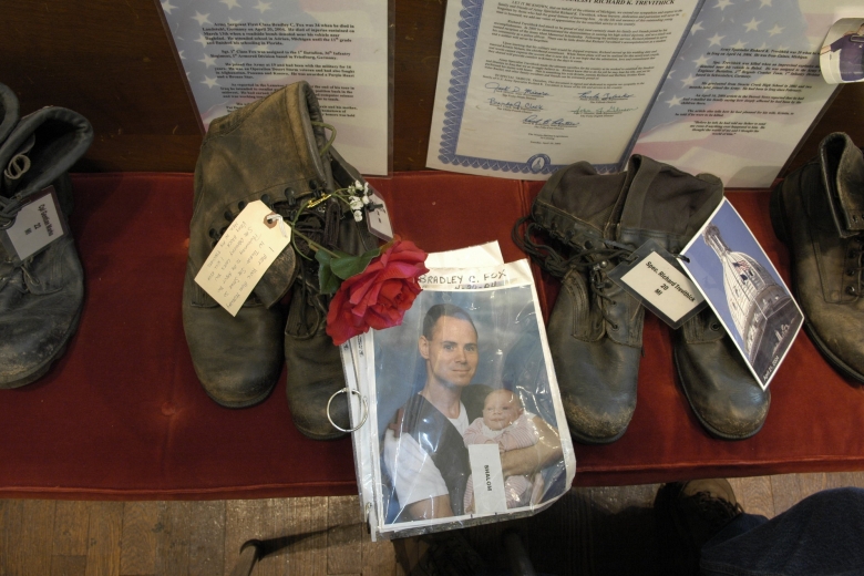 Pairs of boots with photos of servicemen, flowers, and documents.