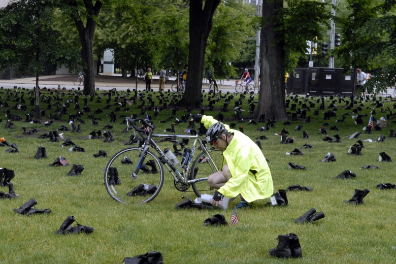Person holding a bike kneels near a pair of boots to read something.