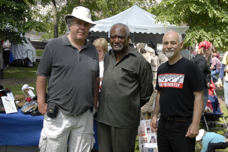 Three men stand next to each other at an outside fair.