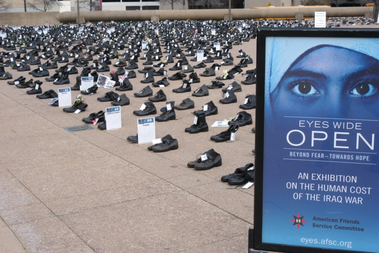 Rows and columns of boots fill a large public area and a sign in front reads "Eyes Wide Open."
