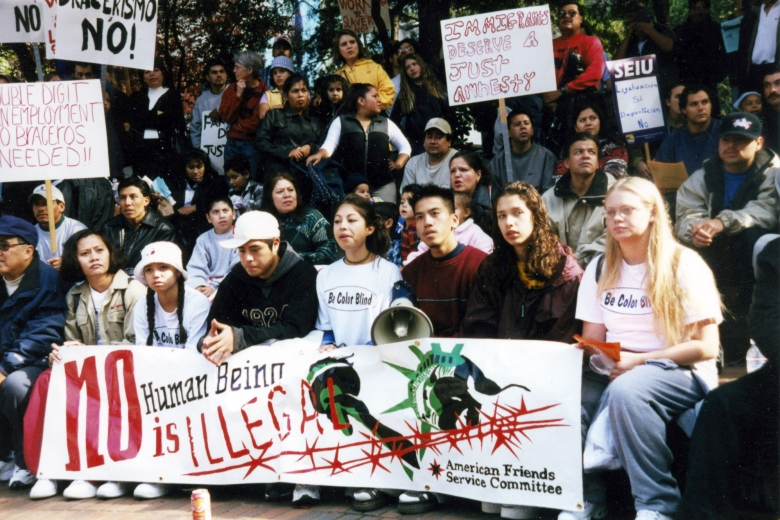 Young adults sit and stand together in a large group holding megaphones and signs.