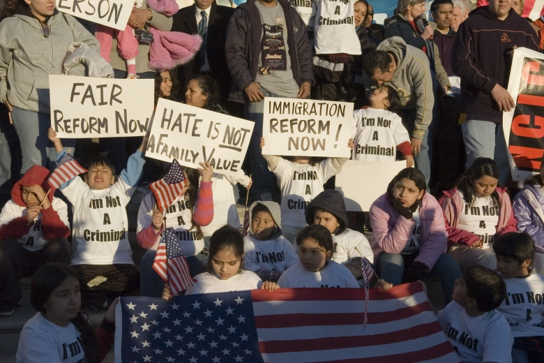 A multi-age group holds signs and a U.S. flag.