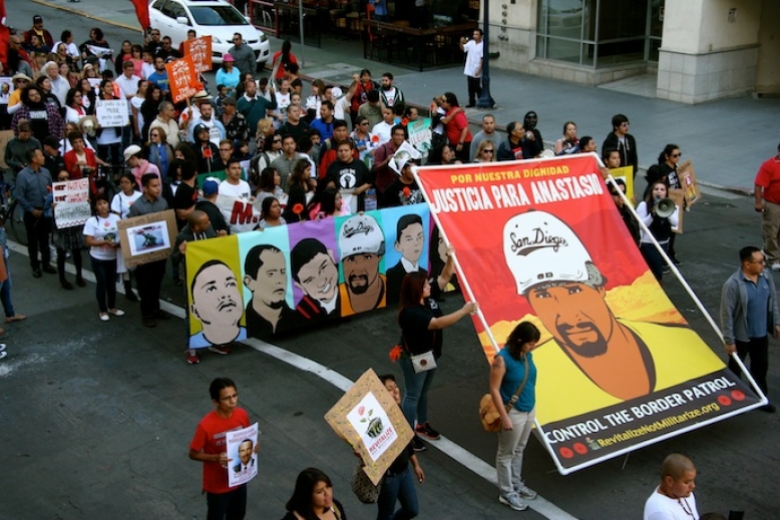 Large group of people march in street holding drawings of men who were killed by border patrol.