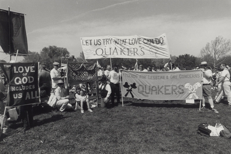 Group of people stand and sit together in a field holding banners about LGBT rights and Quakers.